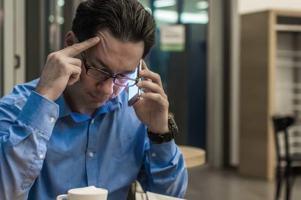 Man experiencing eye discomfort, holding his temple and talking on the phone.
