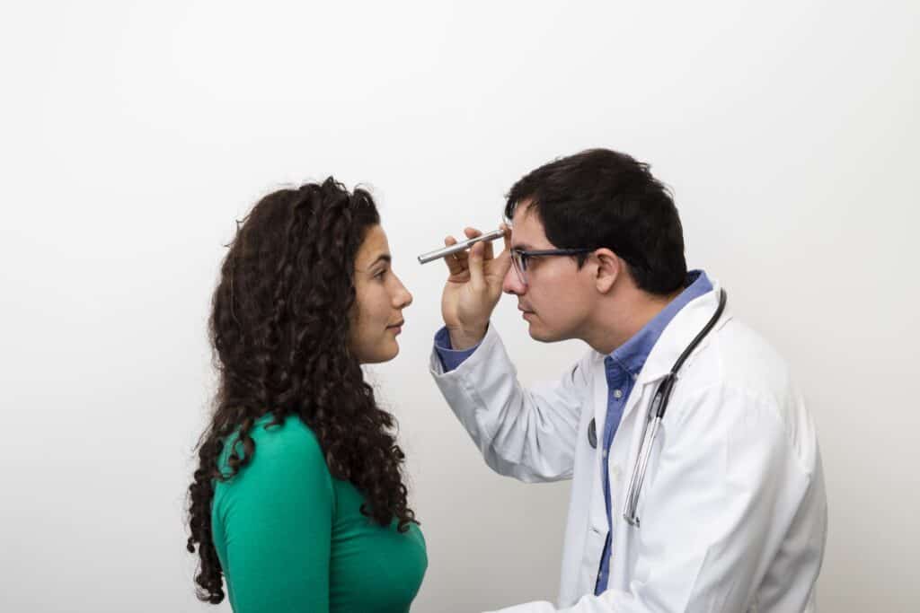 Doctor examining young woman's eyes with an ophthalmoscope in clinic.