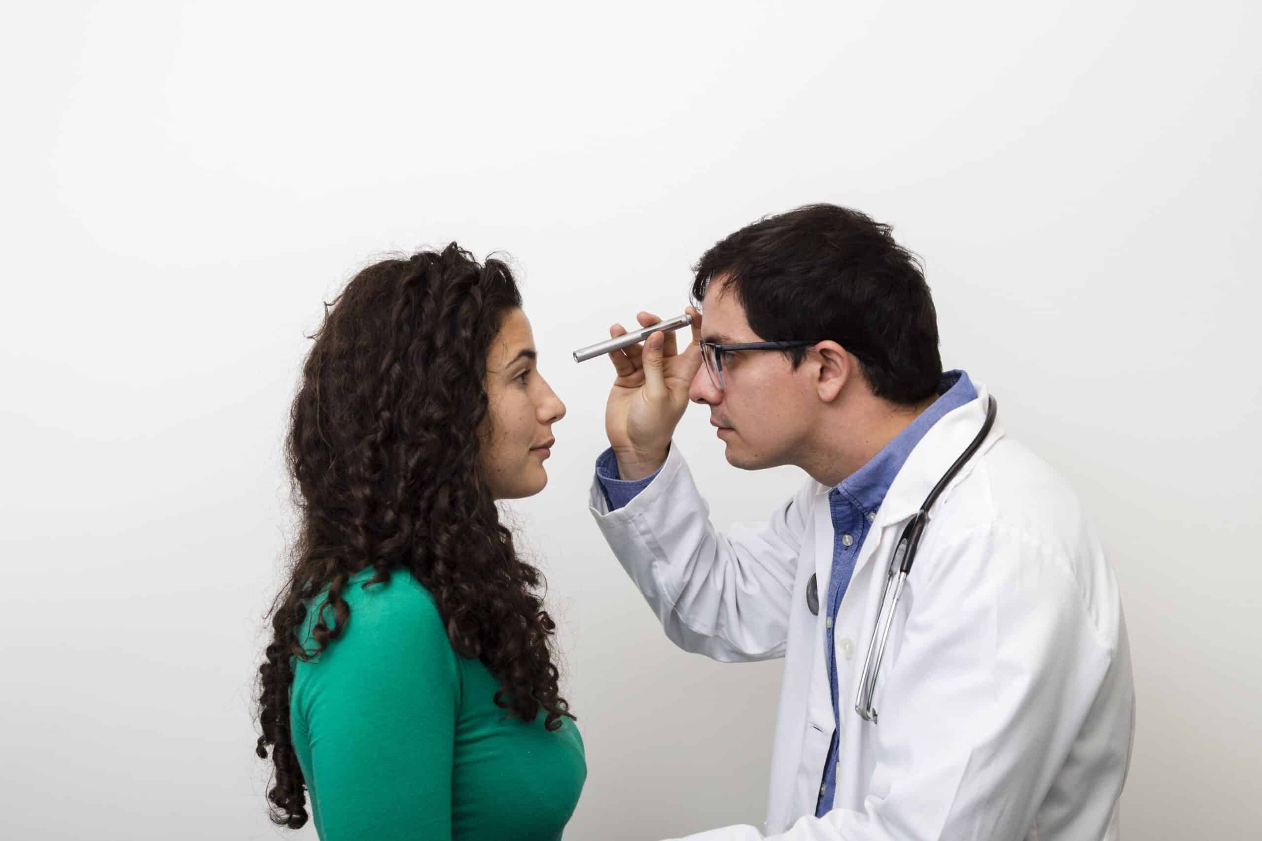 Doctor examining young woman's eyes with an ophthalmoscope in clinic.